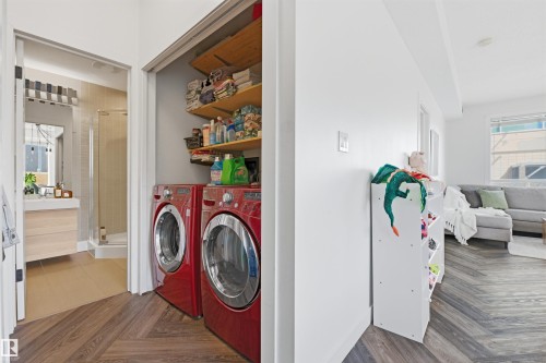 Laundry closet featuring a stackable washer and dryer, wood shelving, and wood-finish flooring - 101 8108 109 Street, Edmonton, AB - Indoor Photo Showing Laundry Room