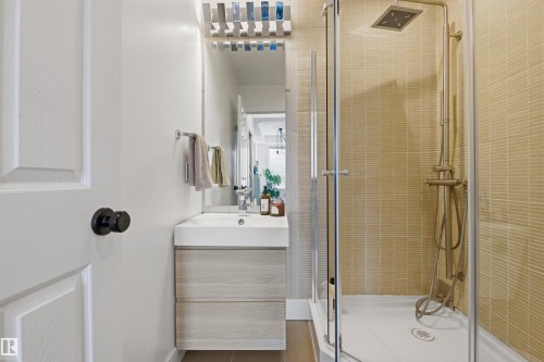 Modern bathroom featuring a glass-enclosed shower with a square rainfall showerhead, beige horizontal tile, and a floating vanity with an integrated sink - 101 8108 109 Street, Edmonton, AB - Indoor Photo Showing Bathroom