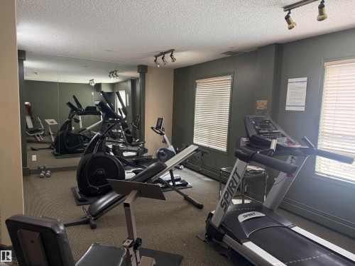 The property features a well-equipped fitness area with various exercise machines, including a treadmill and an elliptical - 101 9760 174 Street, Edmonton, AB - Indoor Photo Showing Gym Room