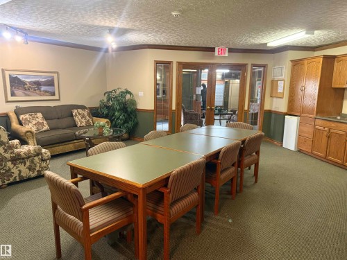 The property offers a versatile communal area featuring carpeted flooring, track lighting, and wainscoting - 101 9760 174 Street, Edmonton, AB - Indoor
