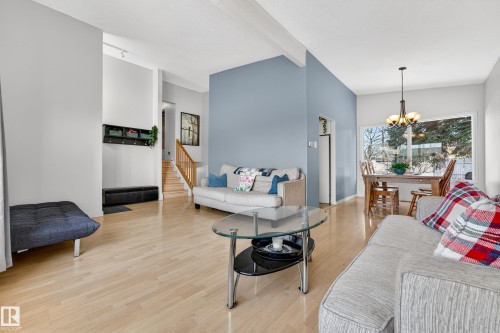 Open-concept living area with light wood-finish flooring, vaulted ceilings with exposed beams, and a prominent blue accent wall - 5304 90A Avenue, Edmonton, AB 