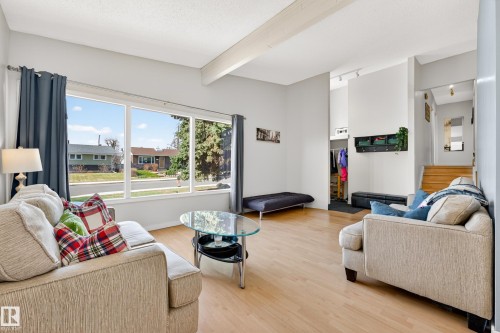 Bright living area featuring expansive windows, wood-finish flooring, vaulted ceilings with exposed beams, and a built-in entry coat closet - 5304 90A Avenue, Edmonton, AB 