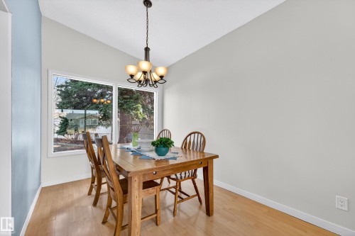 Dining area featuring wood-finish flooring, a large window, a vaulted ceiling, and a chandelier with amber-toned shades - 5304 90A Avenue, Edmonton, AB 