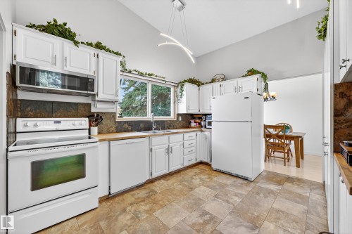 Kitchen featuring white cabinetry, stone backsplash, and wood-finish countertops - 5304 90A Avenue, Edmonton, AB 