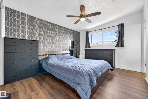 Bedroom featuring wood-finish flooring, a geometric accent wall, and a ceiling fan - 5304 90A Avenue, Edmonton, AB 