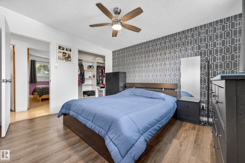 Bedroom featuring wood-finish flooring, a contemporary patterned accent wall, and a ceiling fan with integrated lighting - 5304 90A Avenue, Edmonton, AB 