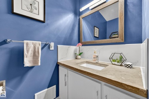 Bathroom vanity featuring a light-toned countertop with an integrated sink, white cabinetry, a framed mirror, and a full-width light fixture - 5304 90A Avenue, Edmonton, AB 