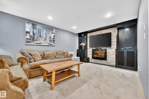 Entertainment wall featuring an integrated linear fireplace set into a stone tile surround, built-in cabinetry, recessed lighting, and a television mount - 5304 90A Avenue, Edmonton, AB 