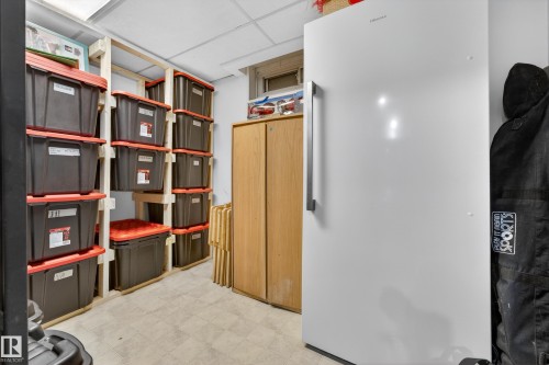 Utility space featuring built-in wooden shelving, a white full-size refrigerator, a light wood-finish storage cabinet, and light-colored flooring - 5304 90A Avenue, Edmonton, AB 