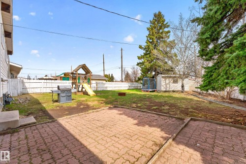 Expansive backyard featuring a red paver patio, a white picket fence, and mature evergreen trees - 5304 90A Avenue, Edmonton, AB 