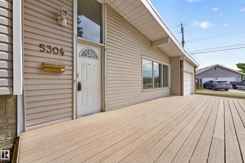 Front facade with horizontal siding, a white entry door featuring an arched fanlight, and an expansive wood-finish deck - 5304 90A Avenue, Edmonton, AB 