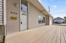 Front facade with horizontal siding, a white entry door featuring an arched fanlight, and an expansive wood-finish deck - 5304 90A Avenue, Edmonton, AB 
