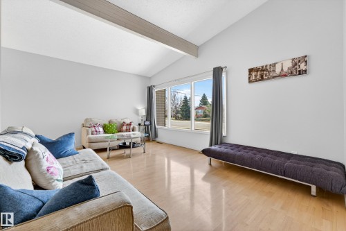 Spacious living area featuring a vaulted ceiling with exposed beam, expansive windows, wood-finish flooring, and light gray wall tones - 5304 90A Avenue, Edmonton, AB 