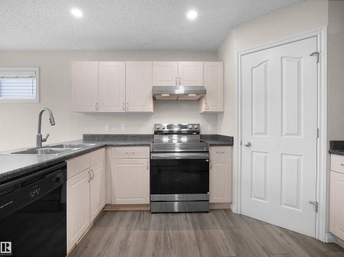Modern kitchen featuring light-toned cabinetry, dark countertops, a stainless steel range with matching hood, a double basin sink with a gooseneck faucet, and wood-finish flooring - 7407 Singer Landing Landing, Edmonton, AB - Indoor Photo Showing Kitchen With Double Sink