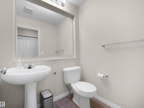 Powder room featuring a pedestal sink, white toilet, and wood-finish flooring - 7407 Singer Landing Landing, Edmonton, AB - Indoor Photo Showing Bathroom