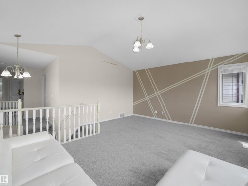 Vaulted ceiling room featuring light gray carpeting, a decorative accent wall, and a window with horizontal blinds - 7407 Singer Landing Landing, Edmonton, AB - Indoor Photo Showing Other Room