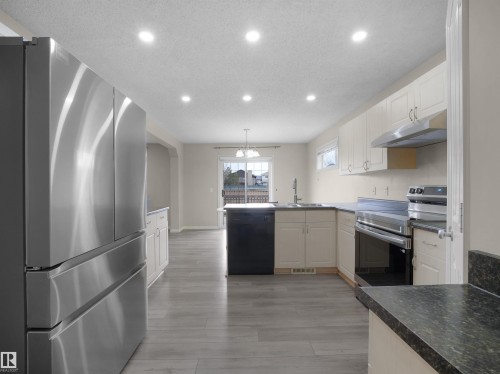Spacious kitchen featuring stainless steel appliances, light-toned cabinetry, dark countertops, recessed lighting, and wood-finish flooring - 7407 Singer Landing Landing, Edmonton, AB - Indoor Photo Showing Kitchen