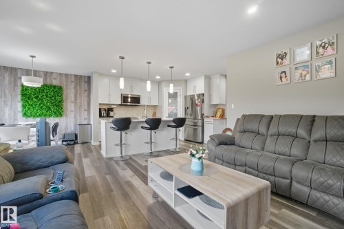 Open-concept living space featuring wood-finish flooring, recessed lighting, white kitchen cabinetry, a kitchen island with pendant lighting, and stainless steel appliances - 2039 Wonnacott Way, Edmonton, AB 