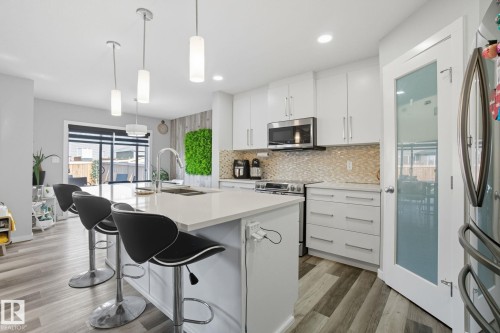 Kitchen featuring a large island with a sink, pendant lighting, white cabinetry, stainless steel appliances, and wood-finish flooring - 2039 Wonnacott Way, Edmonton, AB 