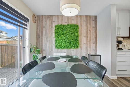 Dining area featuring wood-finish accent wall with a unique green art piece, a contemporary ceiling light fixture, and large sliding glass doors opening to a wood-decked patio - 2039 Wonnacott Way, Edmonton, AB 