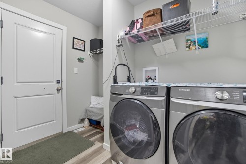 Dedicated laundry area featuring front-loading appliances, overhead wire shelving, and wood-finish flooring - 2039 Wonnacott Way, Edmonton, AB 