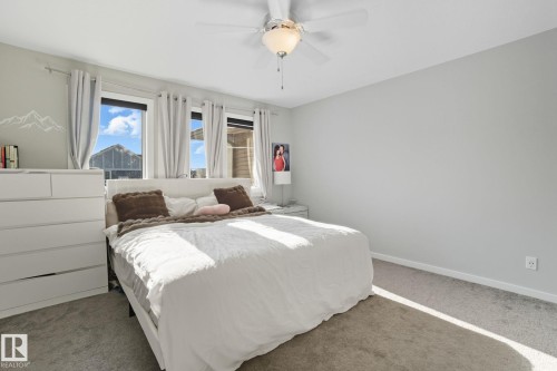 Bedroom featuring three windows, a ceiling fan with integrated lighting, and neutral carpeting - 2039 Wonnacott Way, Edmonton, AB 