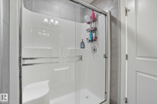 Modern shower enclosure with clear glass doors, chrome hardware, and a built-in bench - 2039 Wonnacott Way, Edmonton, AB 