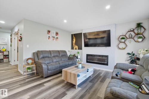 Living area featuring wood-finish flooring, recessed lighting, and a wall-mounted electric fireplace with a textured accent wall - 2039 Wonnacott Way, Edmonton, AB 