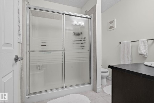 Bathroom featuring a shower with sliding frosted glass doors, light-colored tiled floors, and a dark vanity with a white sink - 1014 162 St Sw, Edmonton, AB - Indoor Photo Showing Bathroom