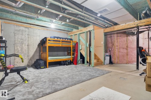 The property features a partially finished basement with exposed wooden beams, concrete walls, and a carpeted section - 1014 162 St Sw, Edmonton, AB - Indoor Photo Showing Basement