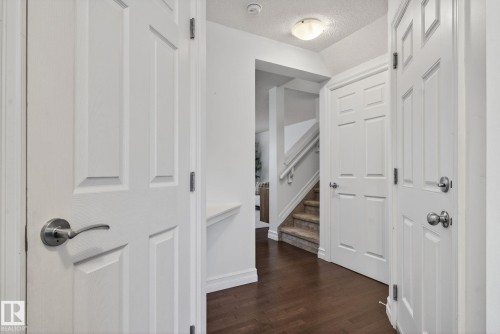 The entrance area features rich hardwood flooring and white paneled doors, leading to a carpeted staircase with white railings - 1014 162 St Sw, Edmonton, AB - Indoor Photo Showing Other Room