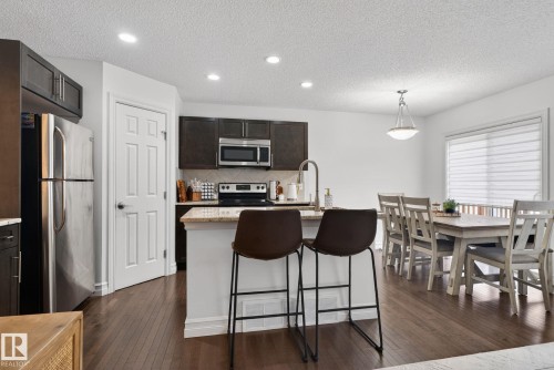 The kitchen features dark cabinetry, stainless steel appliances, and a central island with a light-toned countertop - 1014 162 St Sw, Edmonton, AB - Indoor