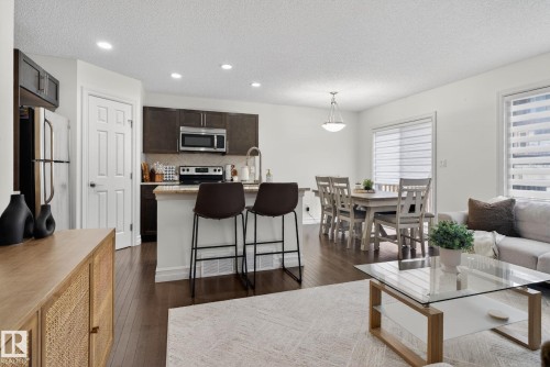 This open-concept living area features hardwood flooring, recessed lighting, and large windows providing natural light - 1014 162 St Sw, Edmonton, AB - Indoor