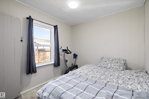 Bright interior room featuring a window with dark curtains, light-toned wall paneling, and wood-finish flooring - 4908 49 Avenue, Onoway, AB - Indoor Photo Showing Bedroom