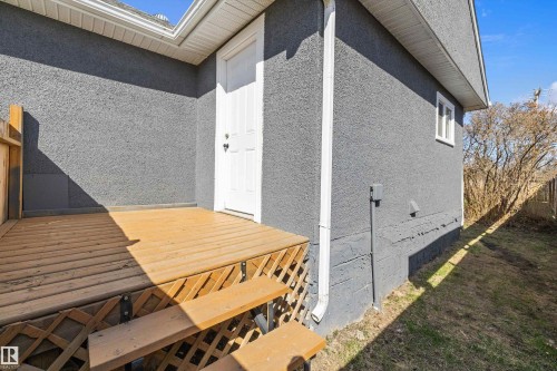 Rear exterior entrance featuring a wood deck with steps, a white door, and gray stucco siding - 4908 49 Avenue, Onoway, AB - Outdoor With Exterior
