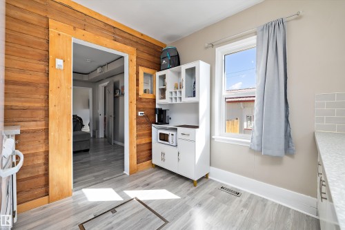 Kitchen area featuring wood-finish accent wall, light wood-finish flooring, white built-in cabinetry with glass inserts, and a single window - 4908 49 Avenue, Onoway, AB -  Photo Showing Other Room