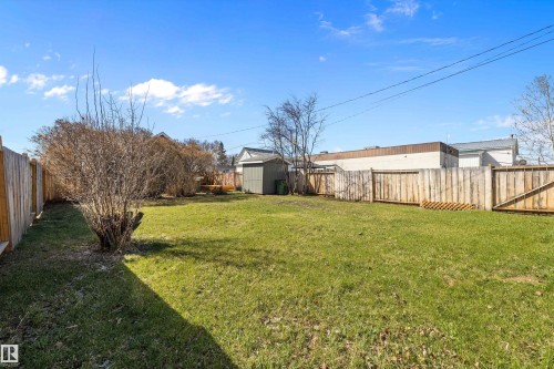 Expansive backyard featuring a spacious lawn, wood fencing, mature shrubs, and an outdoor storage shed - 4908 49 Avenue, Onoway, AB - Outdoor