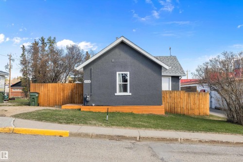 Gray stucco exterior featuring a white-trimmed window, a new wooden privacy fence, a wooden deck, asphalt shingle roofing, and a front yard with grass - 4908 49 Avenue, Onoway, AB - Outdoor