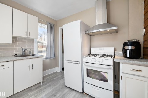 Kitchen featuring white cabinetry, wood-finish flooring, a stainless steel range hood, subway tile backsplash, and a white gas range with oven - 4908 49 Avenue, Onoway, AB - Indoor Photo Showing Kitchen