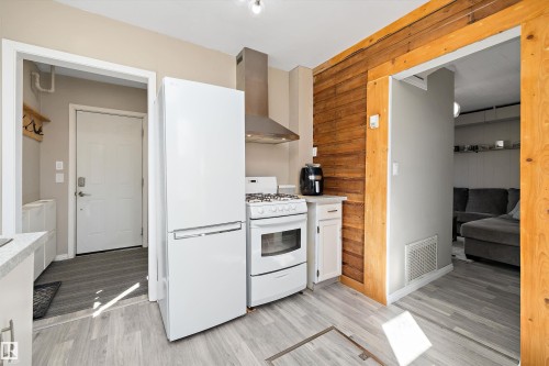 Kitchen featuring light wood-finish flooring, white appliances, a stainless steel range hood, white cabinetry, and a wood-paneled accent wall - 4908 49 Avenue, Onoway, AB - Indoor Photo Showing Kitchen