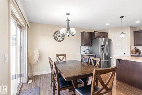 Open-concept dining area featuring wood-finish flooring, a contemporary chandelier, and a sliding glass door - 6864 Evans Wynd, Edmonton, AB - Indoor Photo Showing Dining Room