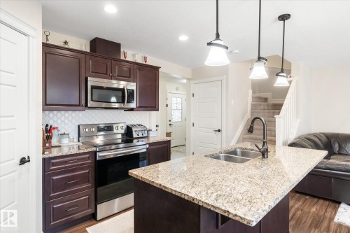 Kitchen featuring granite countertops, dark wood-finish cabinetry, stainless steel appliances, a tile backsplash, and a double basin sink with a gooseneck faucet - 6864 Evans Wynd, Edmonton, AB - Indoor Photo Showing Kitchen With Double Sink With Upgraded Kitchen