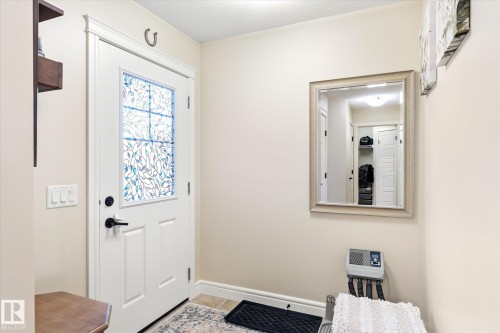 Entryway featuring a white paneled door with decorative glass insert, dark hardware, and a framed wall mirror - 6864 Evans Wynd, Edmonton, AB - Indoor Photo Showing Other Room