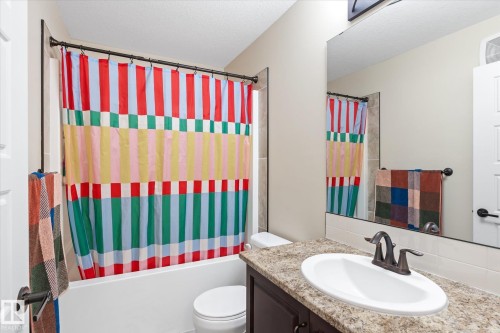 Bathroom featuring a drop-in tub with shower, a vanity with an integrated sink, a large wall-mounted mirror, and a toilet - 6864 Evans Wynd, Edmonton, AB - Indoor Photo Showing Bathroom