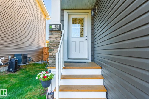 Front entry featuring a white paneled door with decorative glass, wood-finish steps with white risers, and a stone veneer column - 6864 Evans Wynd, Edmonton, AB - Outdoor With Exterior