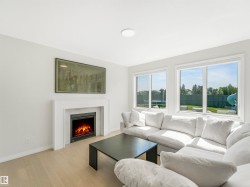 The living area features light-toned flooring, a modern fireplace with a white mantel, and large windows offering views of the outdoors - 