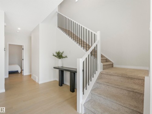 Entryway featuring light hardwood flooring, a carpeted staircase with white and black railings, and white walls - 19 Nettle Crescent, St. Albert, AB - Indoor Photo Showing Other Room