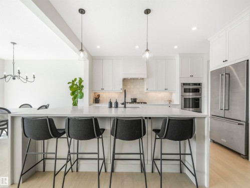 The kitchen features white cabinetry, a large island with seating, stainless steel appliances, and pendant lighting - 19 Nettle Crescent, St. Albert, AB - Indoor Photo Showing Kitchen With Upgraded Kitchen