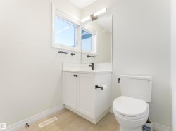 Bathroom featuring a white vanity with dark hardware, a white toilet, and a window providing natural light - 