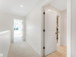 An inviting hallway with light-colored carpeting, white walls, and a recessed ceiling light - 